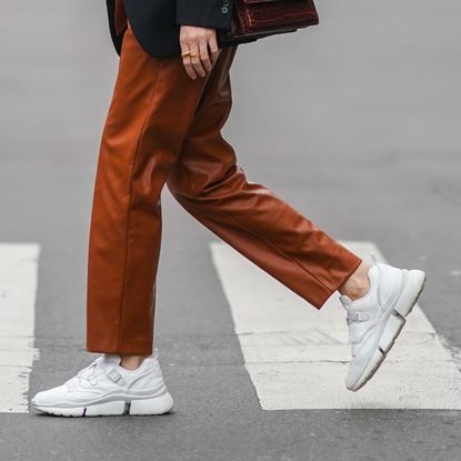 Olesya Senchenko wears earrings, a necklace, a white t-shirt, a black oversized blazer jacket from Lanvin, a brown leather crocodile pattern YSL Saint-Laurent bag, brown leather pants from Antik Batik, white sneakers shoes from Chloe, on February 22, 2021 in Paris, France.