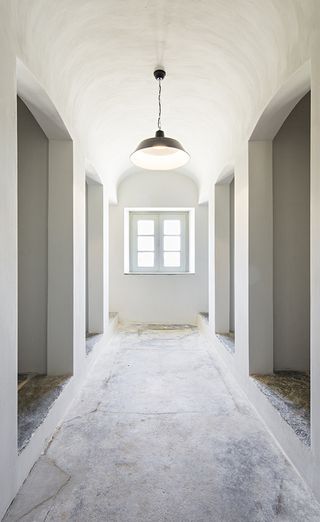 A hallway in the São Lourenço do Barrocal hotel. White walls with a domed ceiling, arched passages to the left and right, and a window to the farthest wall in the center.