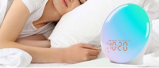 The image shows the JALL sunrise alarm clock on a bedside table in a bedroom 