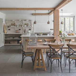 white and wood rustic kitchen with large kitchen island, open plan shelving, rustic table with chairs, pendant lights, stone flooring