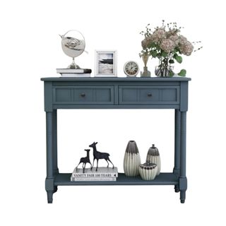 A dark blue console table with decor on top of it and on the open shelf at the bottom of it