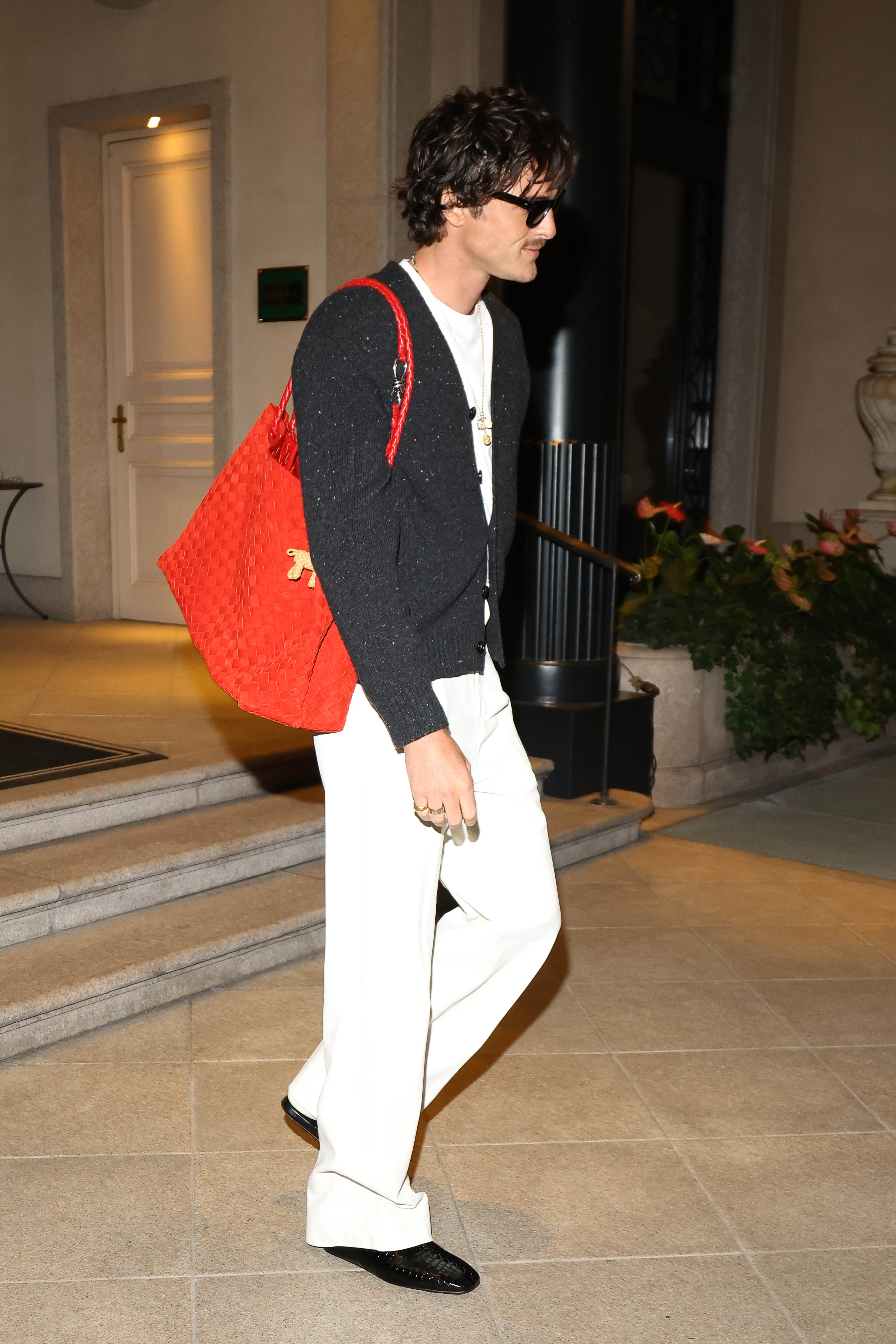 An image of Jacob Elordi wearing an oversized Bottega Veneta bag, white trousers and a black cardigan while out in Venice.