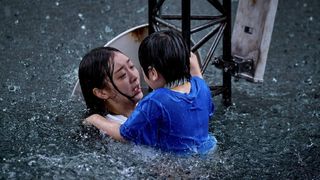 A woman (Kim Da-mi) holds a child as they hold on to an antenna tower during a massive flood, in 'The Great Flood.'