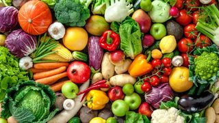 colorful vegetables and fruits including carrots, cucumbers, peppers, eggplant and tomatoes all piled together and viewed from above