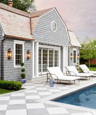 grey barn style garden room next to a pook with checkerboard patio floor