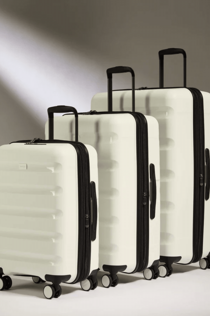 A rotating gif of a white and black suitcase set positioned against a white background, seen open and closed.