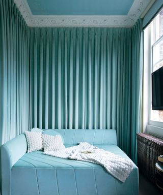 Guest room with light turquoise velvet square sofa bed with diagonal seams, and pleated curtain around the walls, blue painted ceiling and white ceiling trim