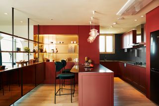 Kitchen in red tones, with illuminated shelving and breakfast bar