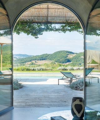 view through glass doors towards swimming pool and hills, with pergola and chairs on terrace