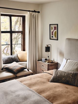 neutral bedroom with alcove window seat, bench, wooden bedside, ochre color palette