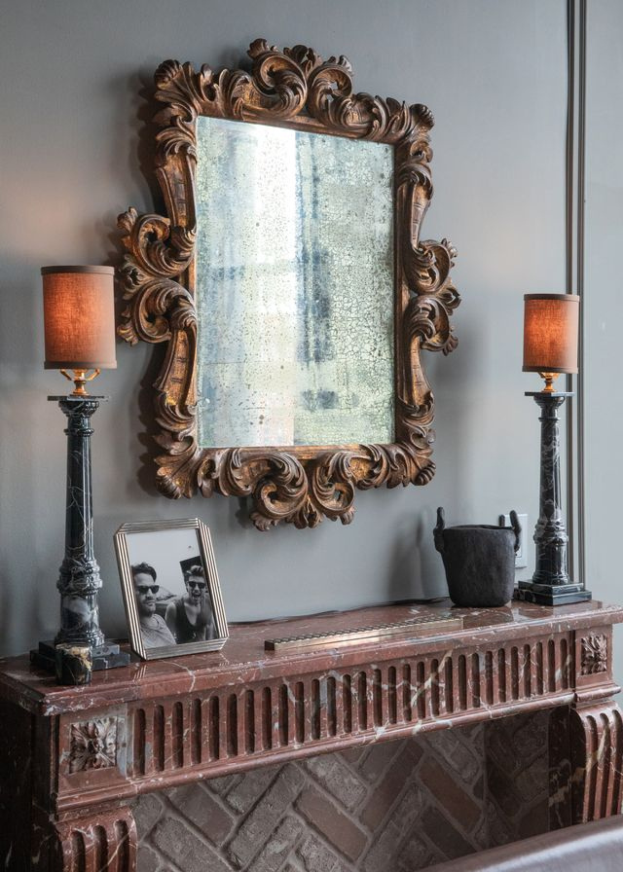 An entryway marble console with an antique mirror hung above and two matching table lamps wither side with a photo frame and decorative item
