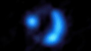 Located centrally on a dark background is an electric blue donut-shaped blob, showing the orientation of the magnetic field of the distant galaxy. The bright donut is not complete, and there are only two main features. The lines of the magnetic field give it an almost furry texture. The right-hand side of the donut forms a bright, curved banana-like shape. Instead, on the left-hand side, there is another bright region, circular in shape.