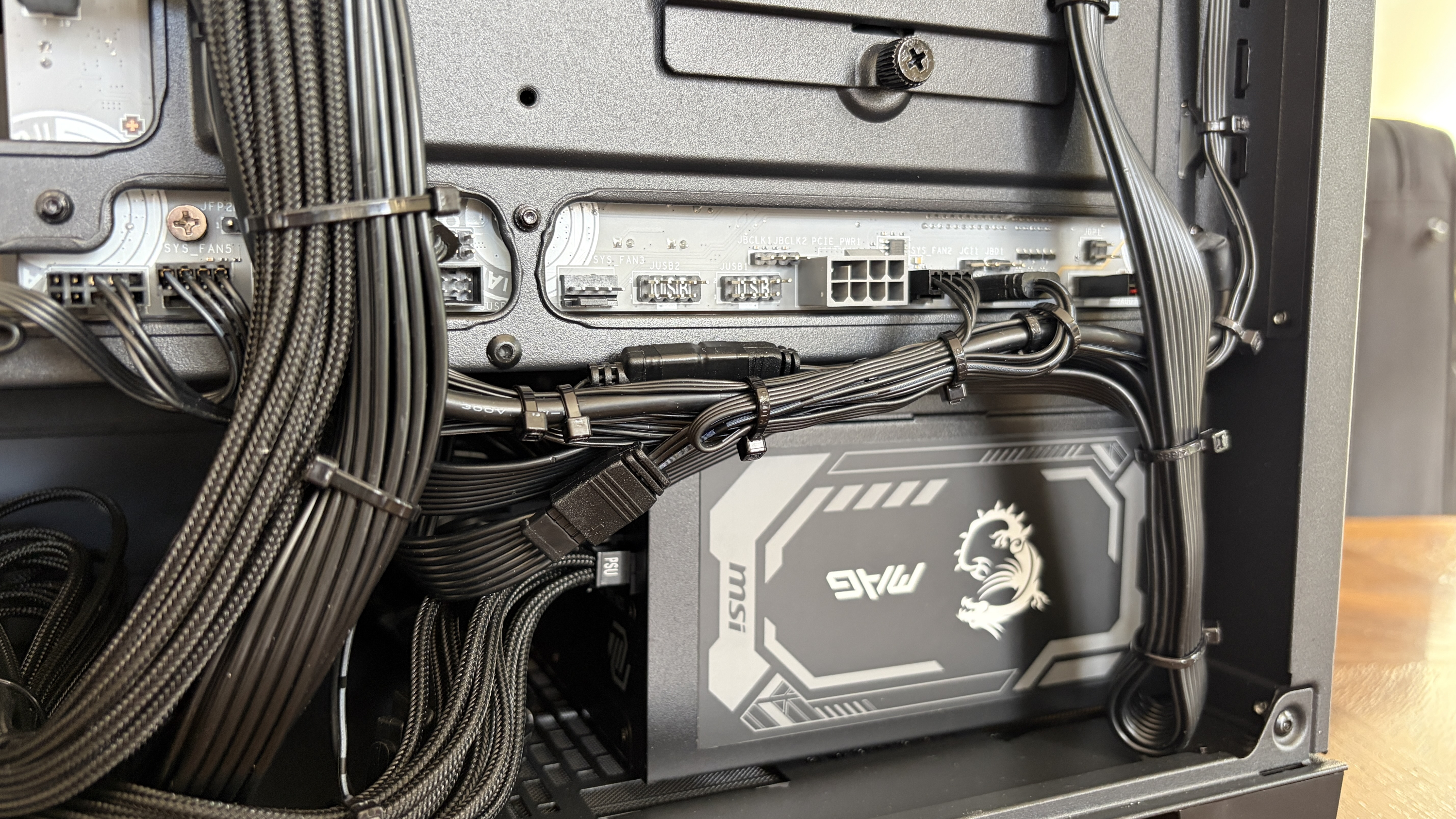 Inside an MG-1 MK.II computer case showing detailed cable management and connections to a PSU with a dragon logo. The setup is neat and organized.