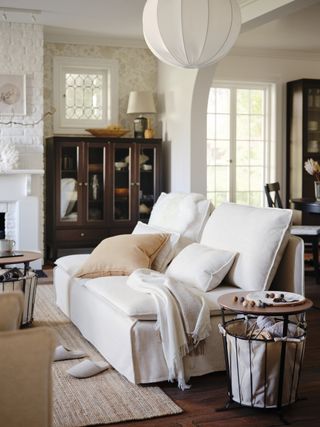 white and neutral living room with white modern style couch, wood and metal storage side tables, neutral rug, taupe cushions, maghogany style display unit