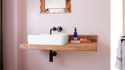 Basin against a pink wall with black bathroom taps