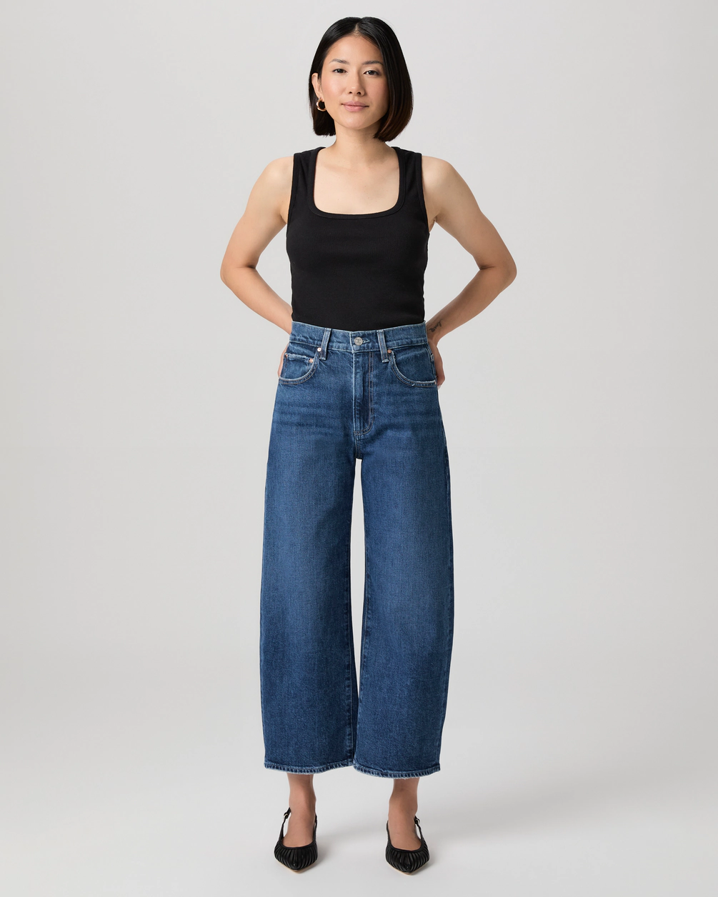 A model wears Paige barrel jeans and black vest top