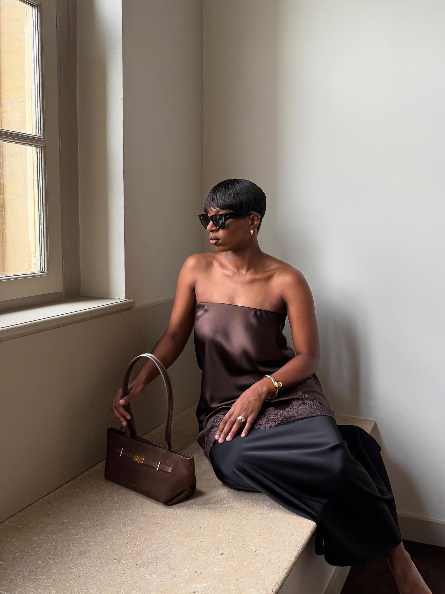 Influencer @thevisuelofgrace wears a satin top with a black satin skirt and brown suede handbag.