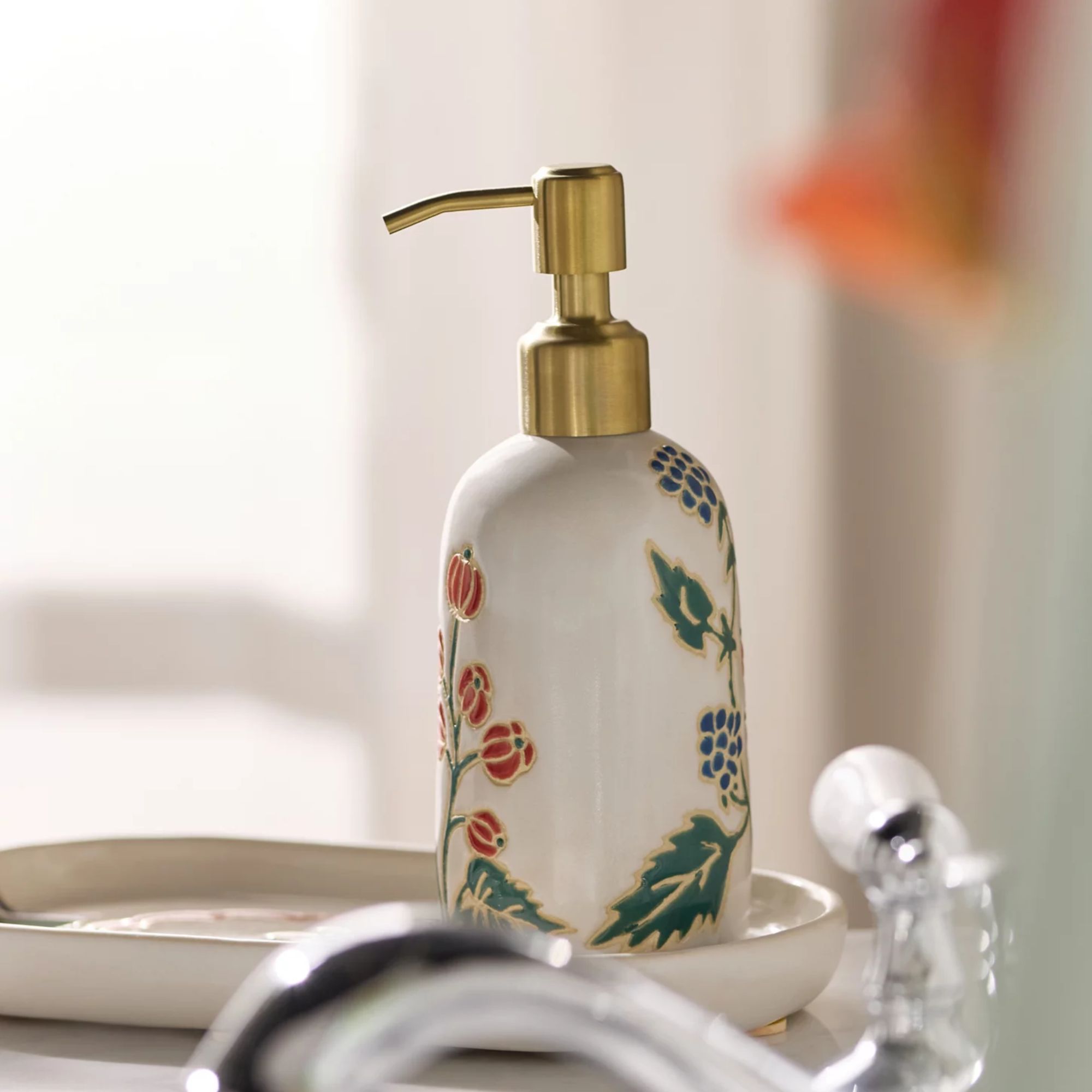 White soap dispenser with red and blue floral design and gold pump