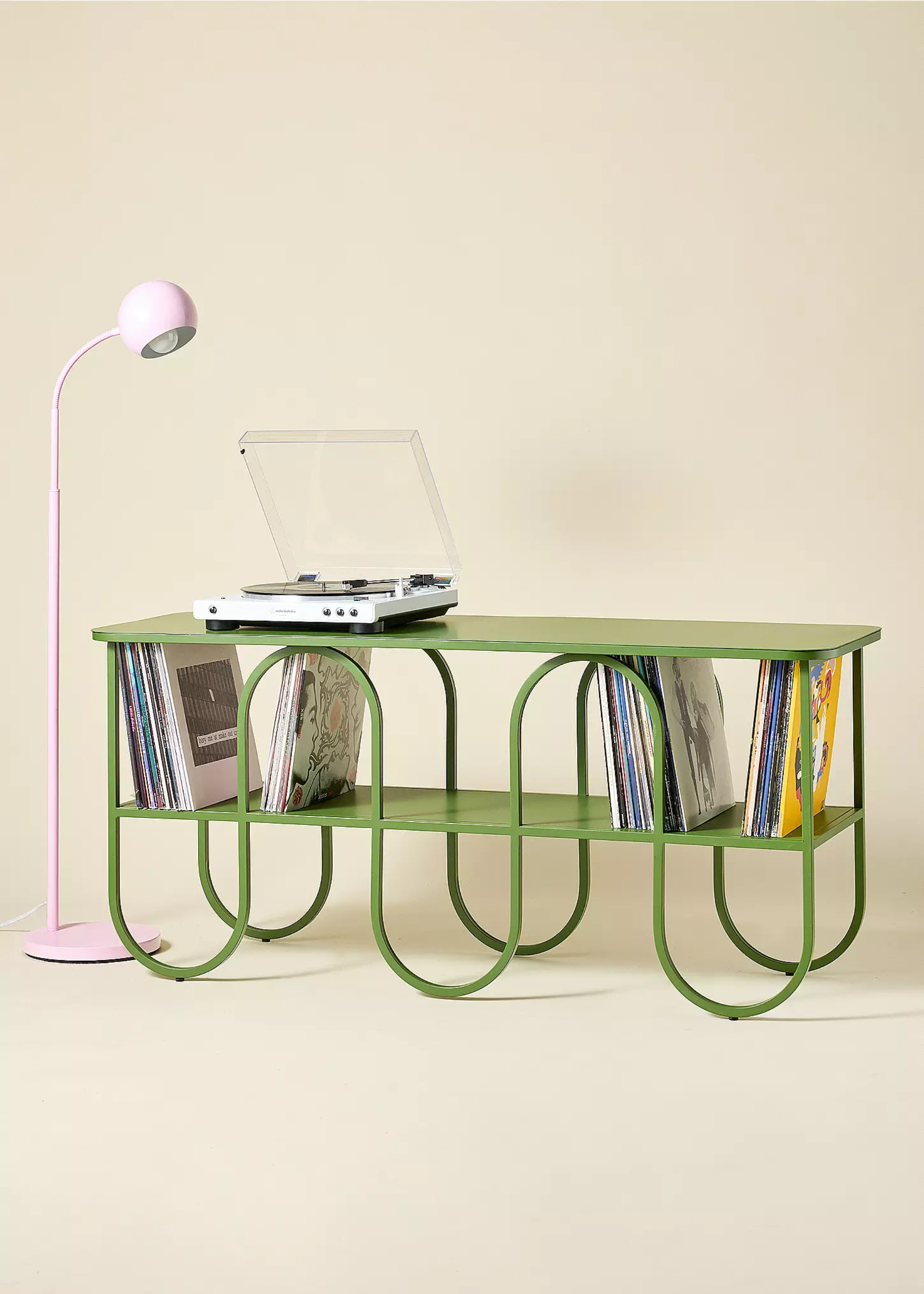 A curved green vinyl holder with a record player and a pink standing lamp