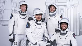 Four humans in white space suits post in front of a white wall with line drawings of a spaceship.