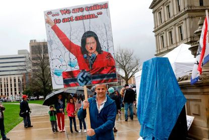 A protester holds a sign depicting Gretchen Whitmer as Adolf Hitler.