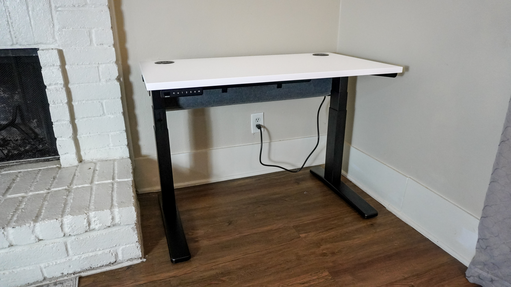 The Uplift V3 standing desk set up in a corner next to a fireplace
