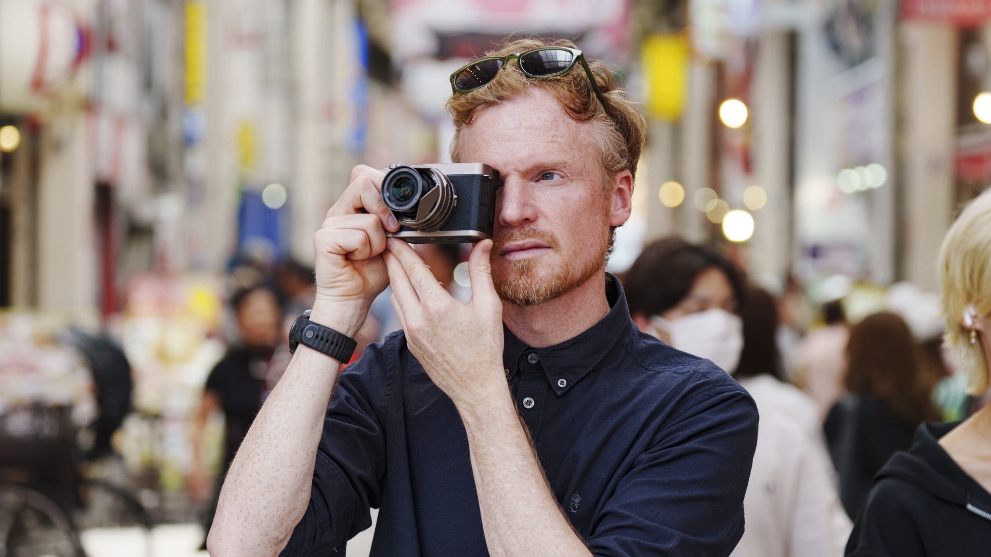 Man holding the Panasonic Lumix L10 compact camera up to his eye, he's looking through the viewfinder, in an urban setting of Japan
