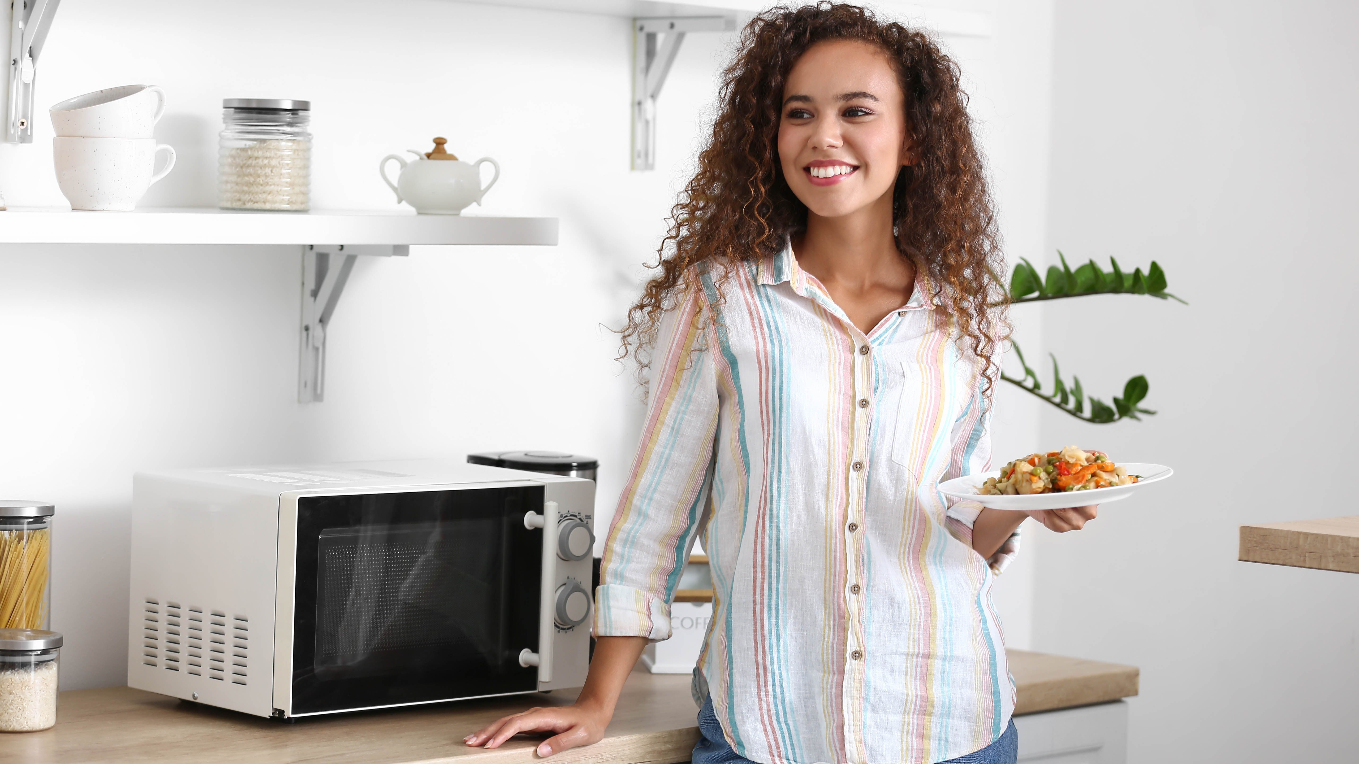 A woman stands next to a microwave with a plate of food