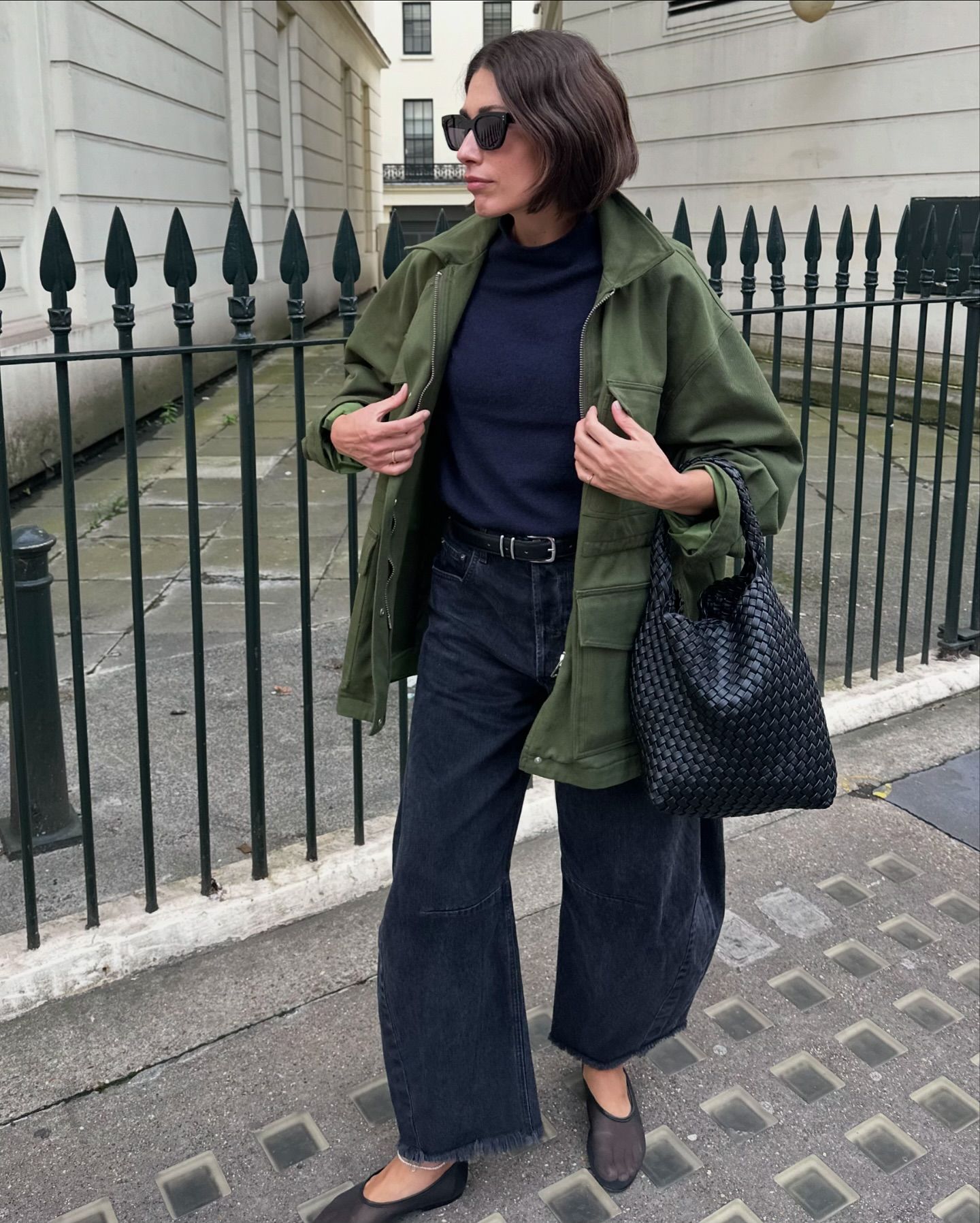 La influencer de moda Lucy Alston en Londres luciendo un elegante conjunto de otoño con jeans negros, zapatos planos de malla, una chaqueta verde y un bolso de cuero Rylan.