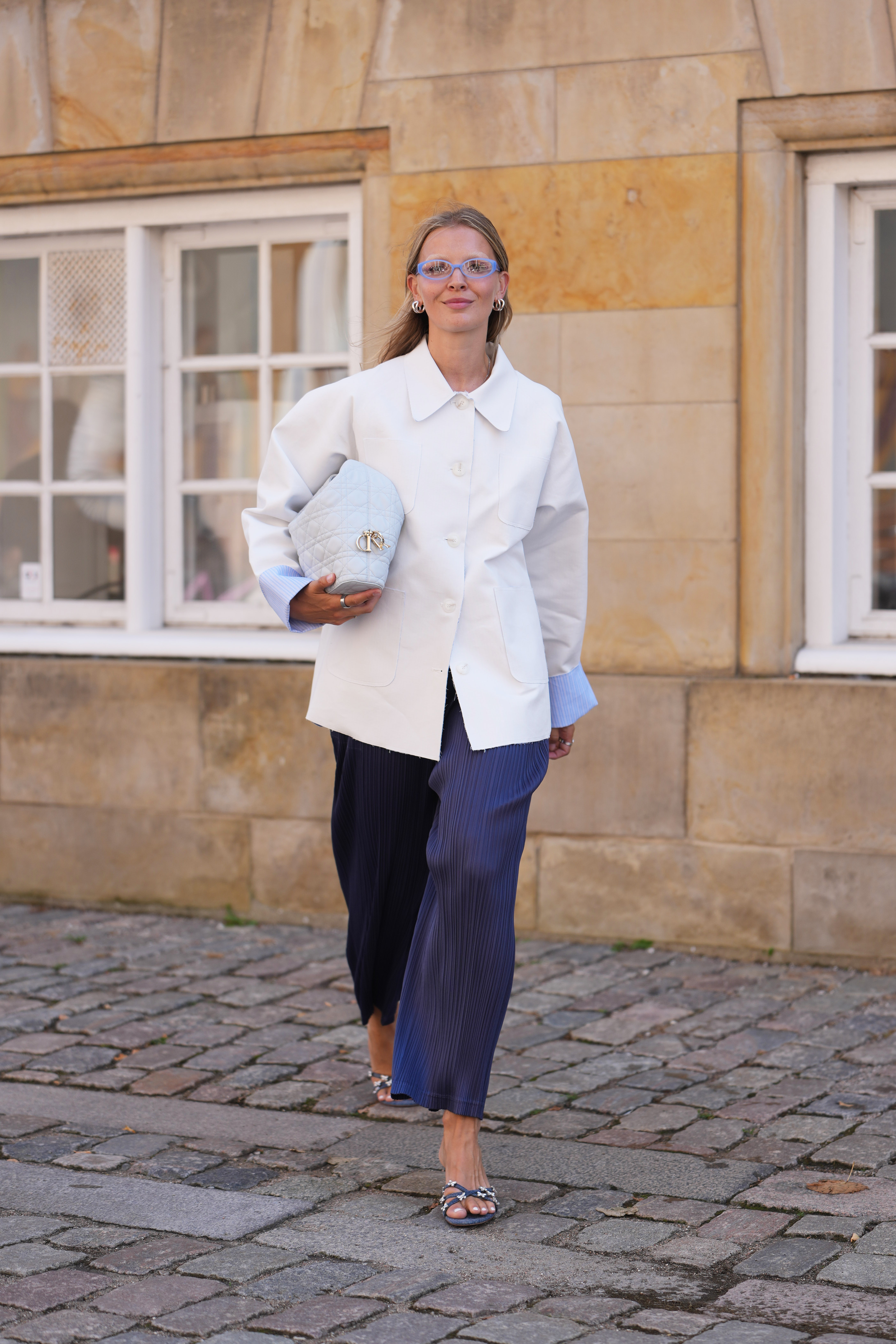 a woman wears a white jacket, white dior bag, purple pants, and embellished heels.
