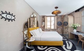 Bedroom featuring mirrored headboard, exposed brickwork, and a bold black and white rug