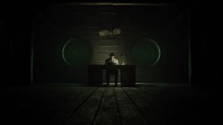 Alan Wake sits at his desk in Alan Wake 2 with dark all around.