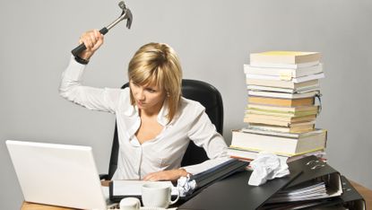 Angry business lady hitting a laptop with a hammer.