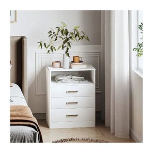 white nightstand with three drawers and one shelf, and books and foliage display on top