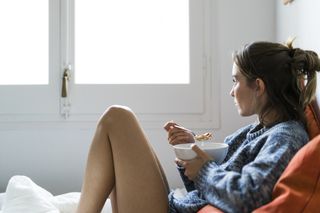 A young woman in bed eating a bowl of cereal