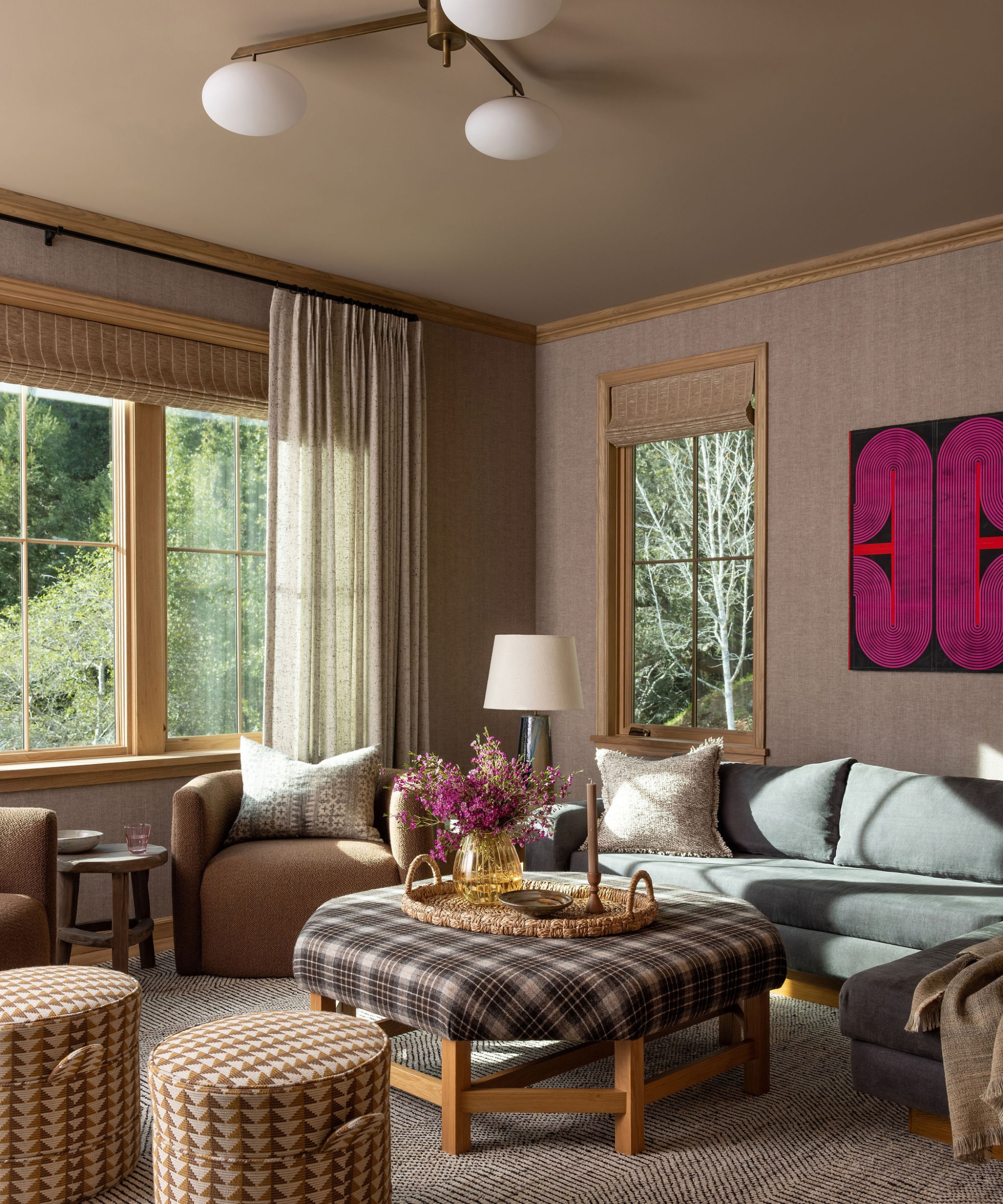 Family room with a blue sofa, tartan ottoman, ochre patterned stools, oak window frames and bright pink geometric artwork.