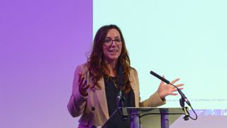 Tricia Troth, general manager at AWS Startup for the UK &amp; Ireland, speaking onstage at the AWS Loft in London. Decorative: Troth is stood at a podium, with a purple and white backdrop.