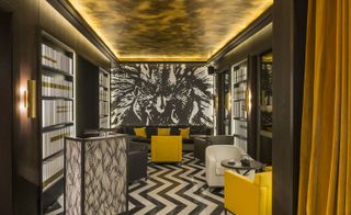 Hexagone "Bookshelf" wall features line the room with mustard draping, mustard, white and dark leather couches for seating
