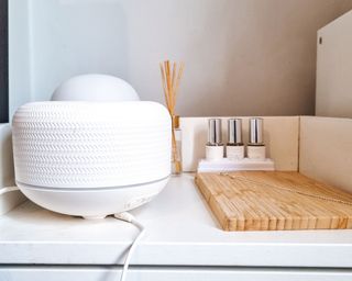 The White Company textured ceramic electronic diffuser on beside table beside wooden board with necklace