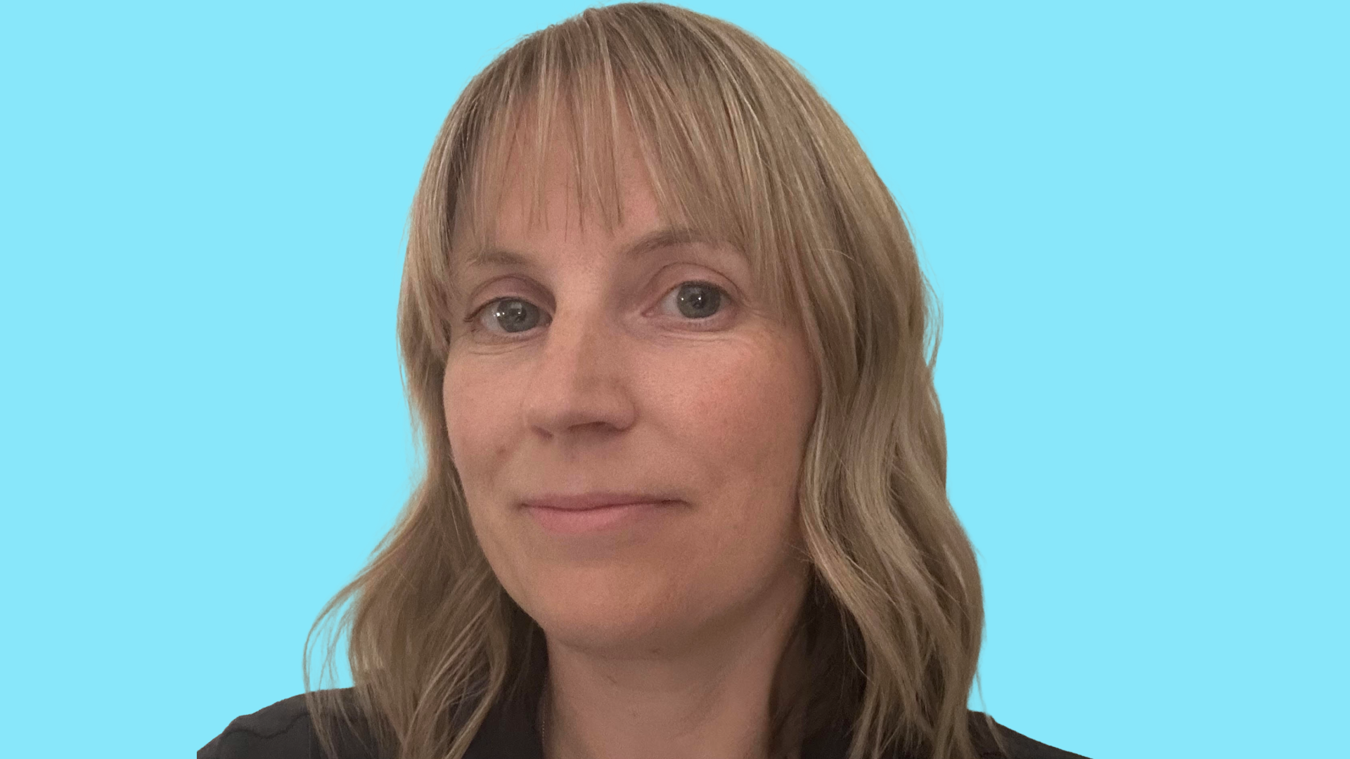 A blonde haired woman, aged 47, smiling, in a black top