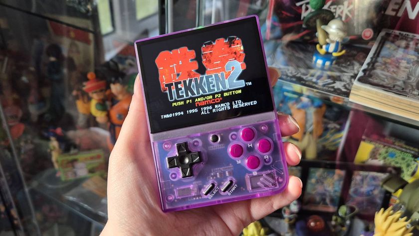 Photo by writer Rosalie Newcombe of their hand holding up the Atomic Purple Miyoo Mini Plus retro gaming handheld infront of a cabinet full of anime toys and figures.