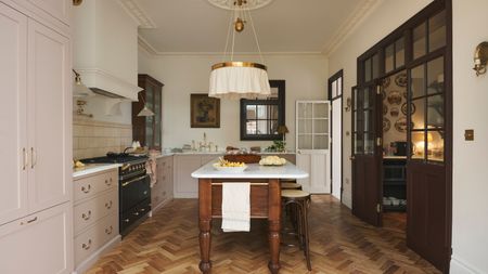 A Victorian home kitchen with cream walls, light pink cabinets, and a large pantry separated by glass doors