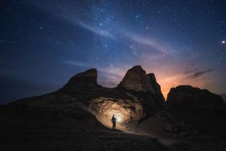 Perseid meteors streak over a striking landscape in China with a person holding a flashlight