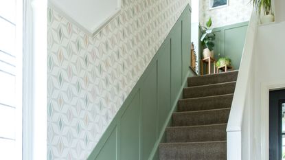 A hallway with a staircase with the bottom half of the walls covered in green wood panelling and the top half covered in wallpaper