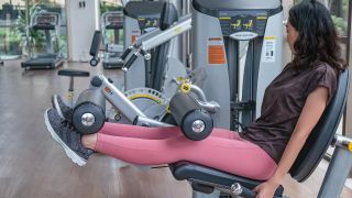 Woman performs leg extension on weights machine in gym