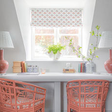 Coral chairs at a desk in front of window with a floral blind.