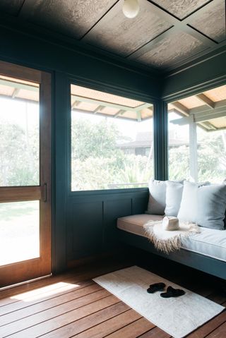 screened in porch with black wood walls and a built in bench with grey cushions