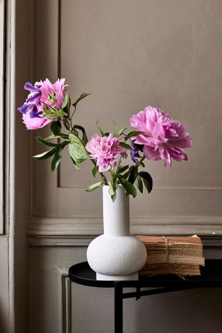 white modern vase with faux peonies on a black side table, vintage books on the side and stone painted panelling