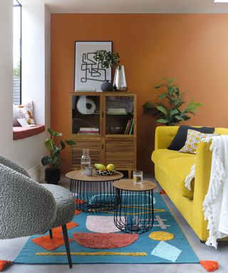 A modern living room with rust / burnt orange wall paint decor and blue abstract pattern rug decor