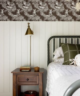 bedroom with white panelled walls with wallpaper above, green bedframe with white bedding and wooden nightstand